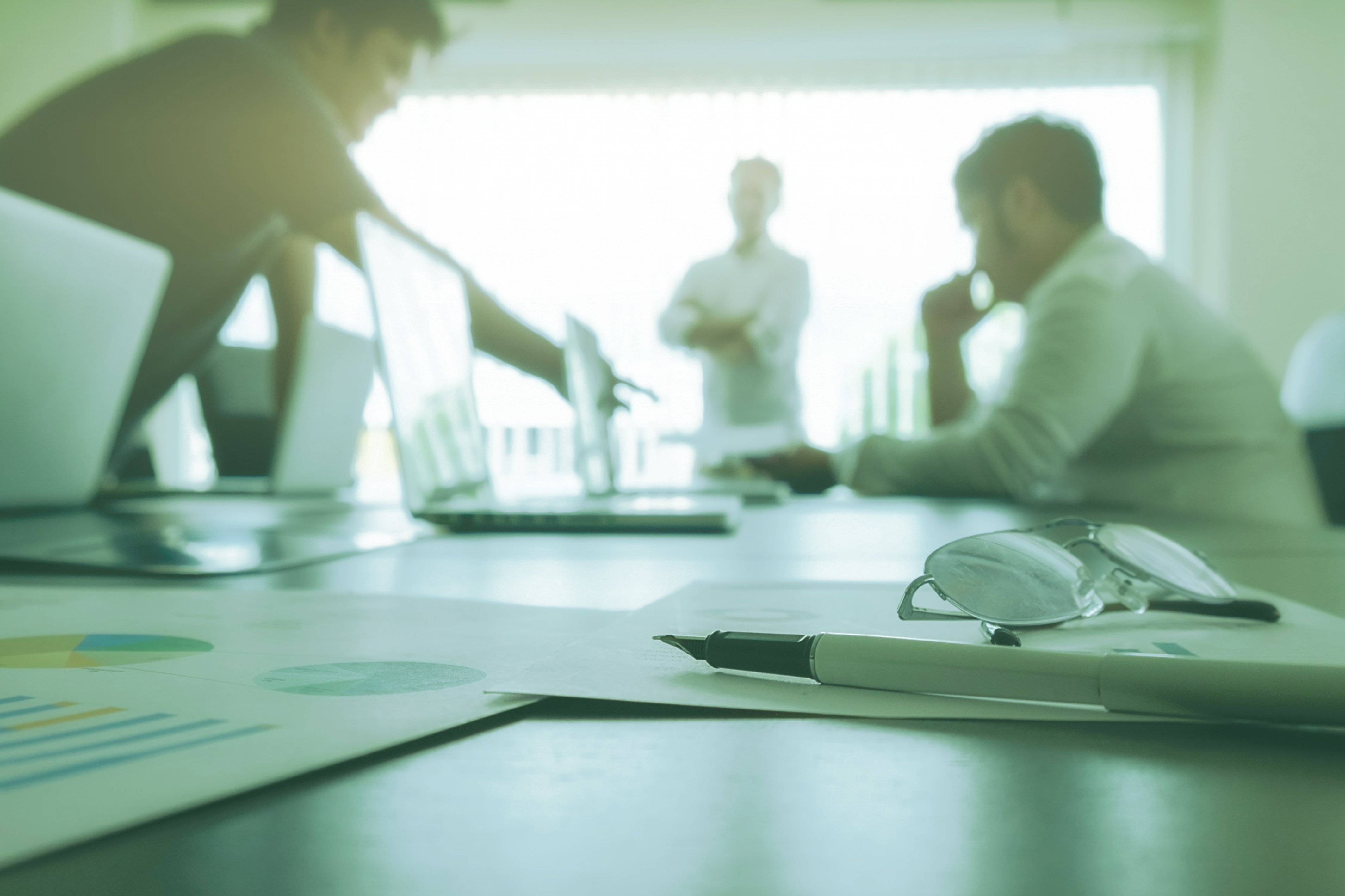 A pen and glasses focused and a team discussing from behind