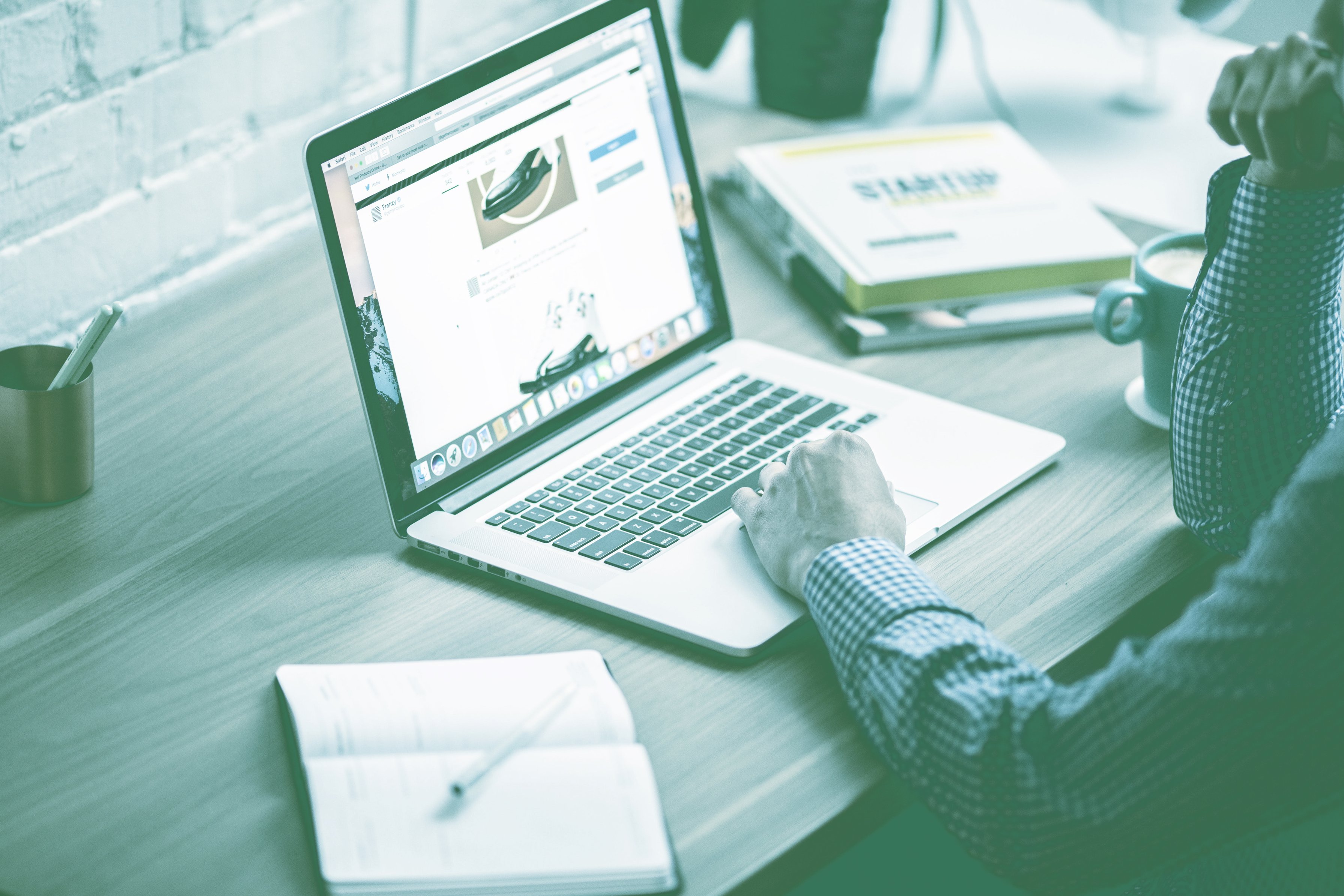 A man's hands navigating a website on his computer while is taking notes